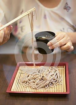 Hand of woman use chopsticks to clamp a noodle on a bamboo dish, japanese noodle, itÃ¢â¬â¢s call Soba, selective focus at noodle